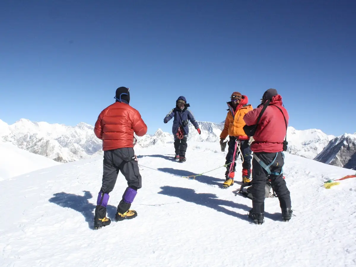 Climbers on Mera Peak’s snowy summit with Himalayan peaks behind them.