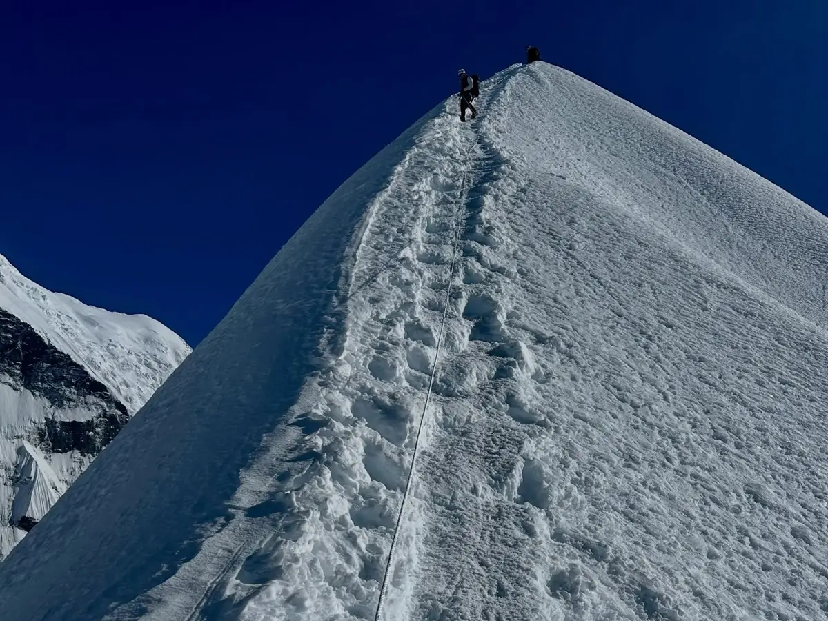 Climbers ascending Island Peak’s narrow, snow-covered summit ridge using a fixed rope