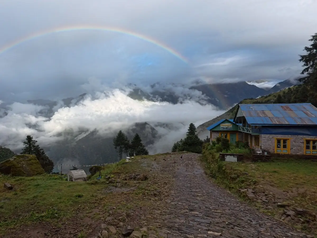 Rainbow above hillside lodges and cloud-covered valleys on the Mera Peak approach trek.