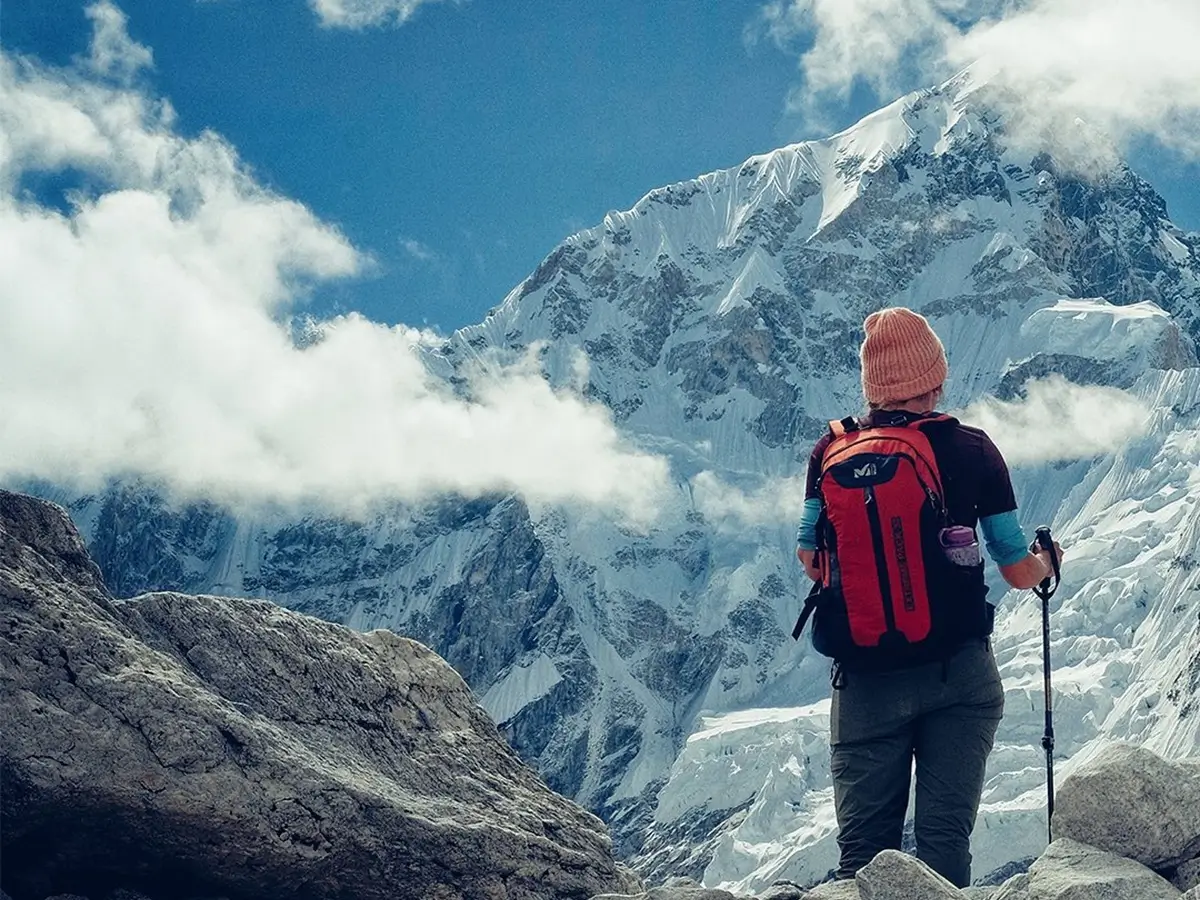 Trekker standing on the rocky Everest Base Camp trail facing a snow-covered Himalayan mountain.