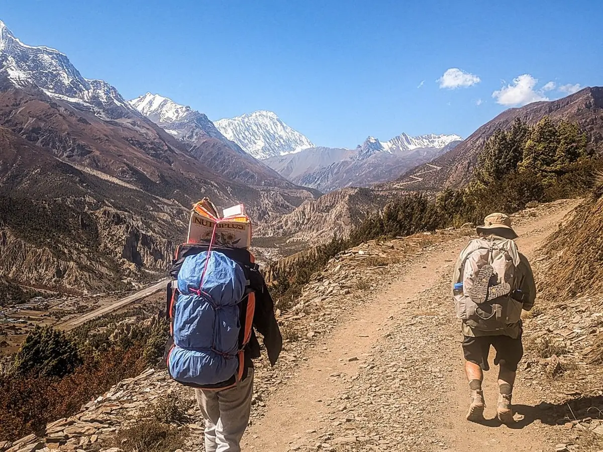 Trekker and porter following a hillside path above a mountain valley on the Annapurna Circuit